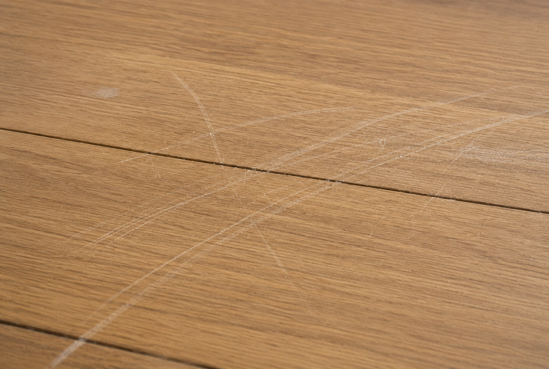 A close-up of scratched and scuffed timber floorboards showing surface wear and damage across the grain.