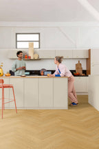 Two people in a modern kitchen with light-colored cabinets and wooden flooring.
