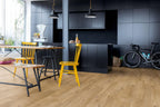 Modern kitchen with black cabinets, wooden floor, and yellow chairs.