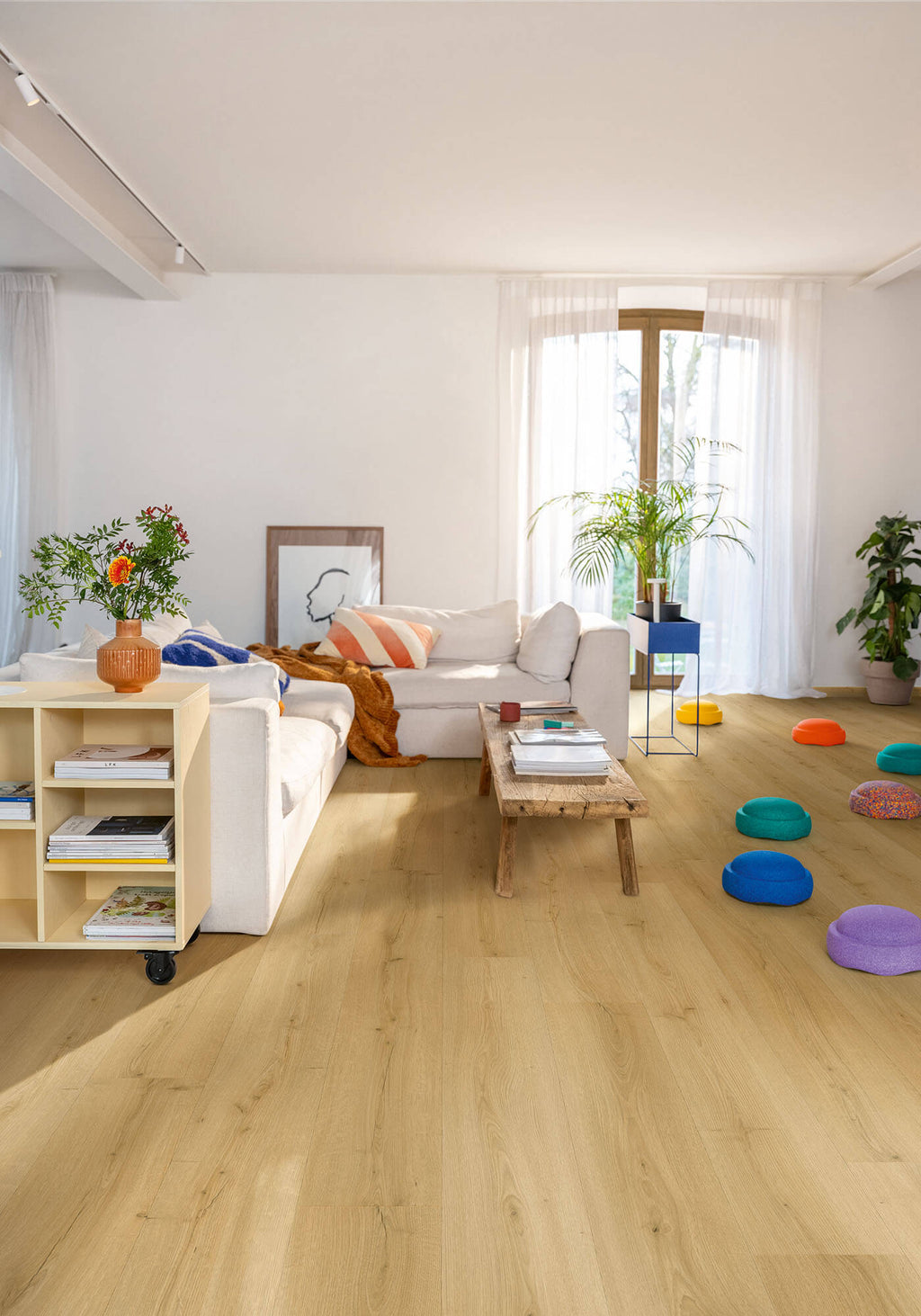 Modern living room with light wood flooring, white walls, and colorful decor items.