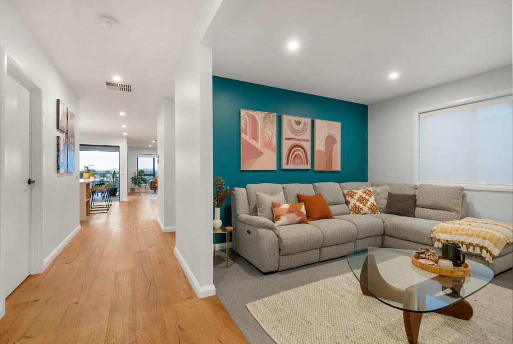 A modern Australian home interior featuring warm Arcadian Oak hardwood timber flooring that flows through a long, bright hallway toward an open-plan living area, complemented by a bold teal feature wall, a generous grey sectional sofa, and earthy terracotta accent cushions for a vibrant, welcoming feel.