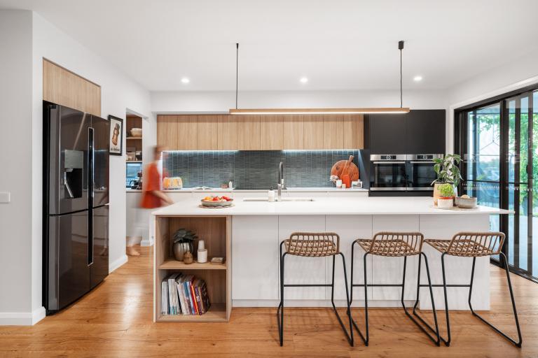 A stylish contemporary kitchen featuring warm Arcadian Oak hardwood timber flooring that ties together the natural oak cabinetry, white stone island bench, teal tile splashback, and woven rattan bar stools for a beautifully cohesive and inviting open-plan space.