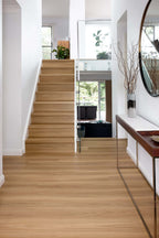 Light oak wood plank flooring in a modern home interior, showing a staircase and hallway with white walls and a console table.