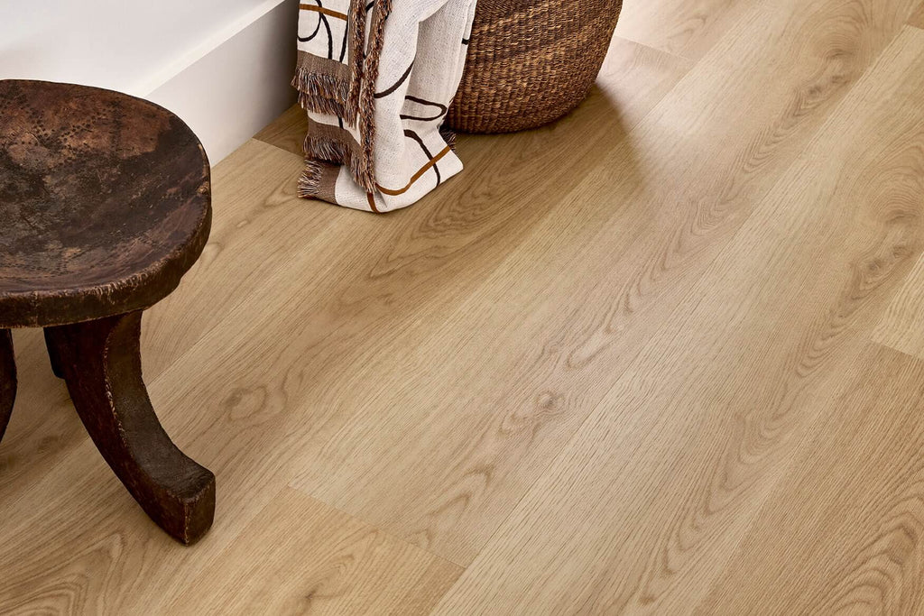 Light oak wood flooring shown in a styled room corner with part of a dark wooden stool and a woven basket visible.