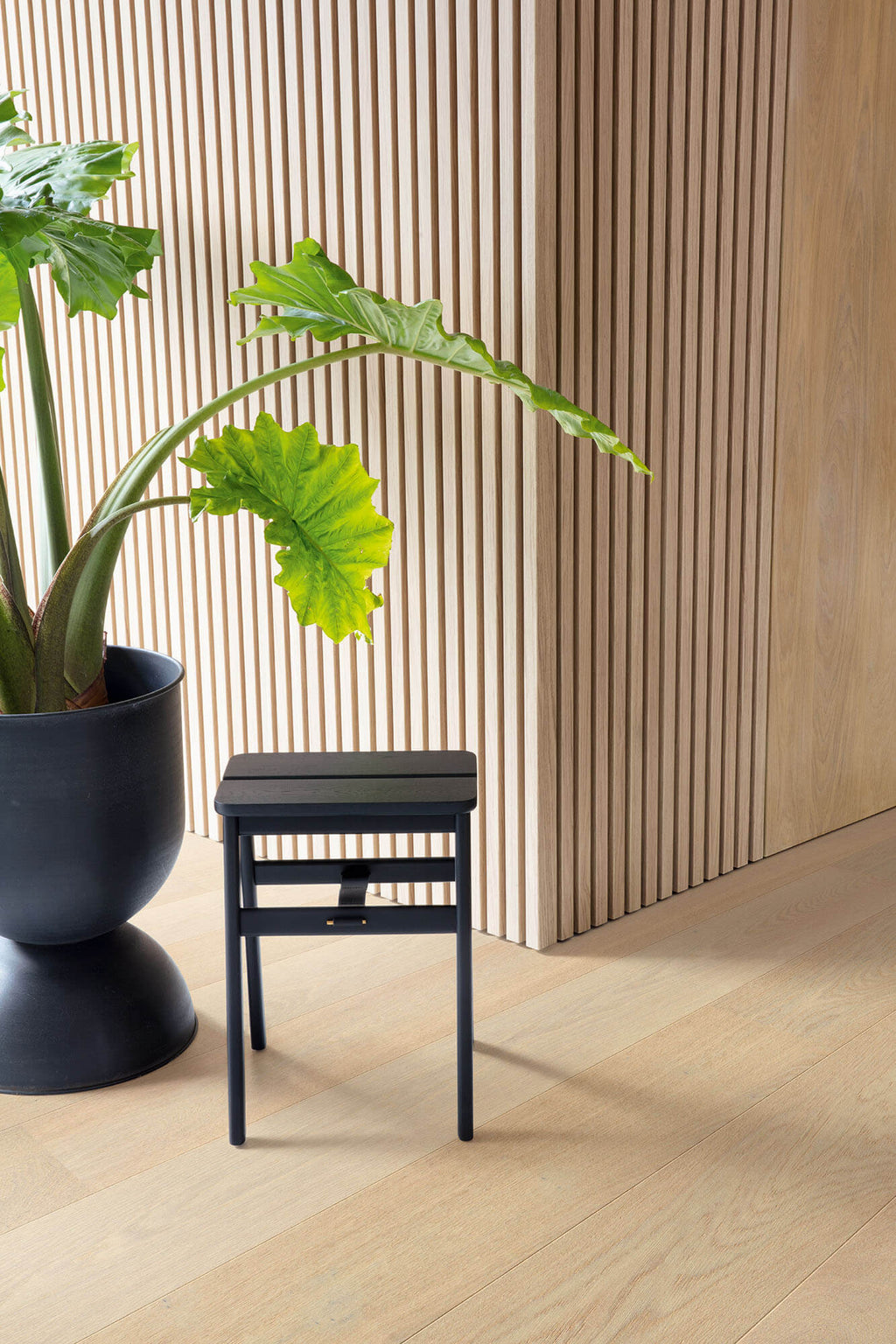 Black stool next to a potted plant against a wooden paneled wall.