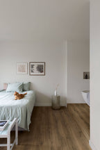 Modern bedroom with a bed, side table, and cat on a wooden floor.