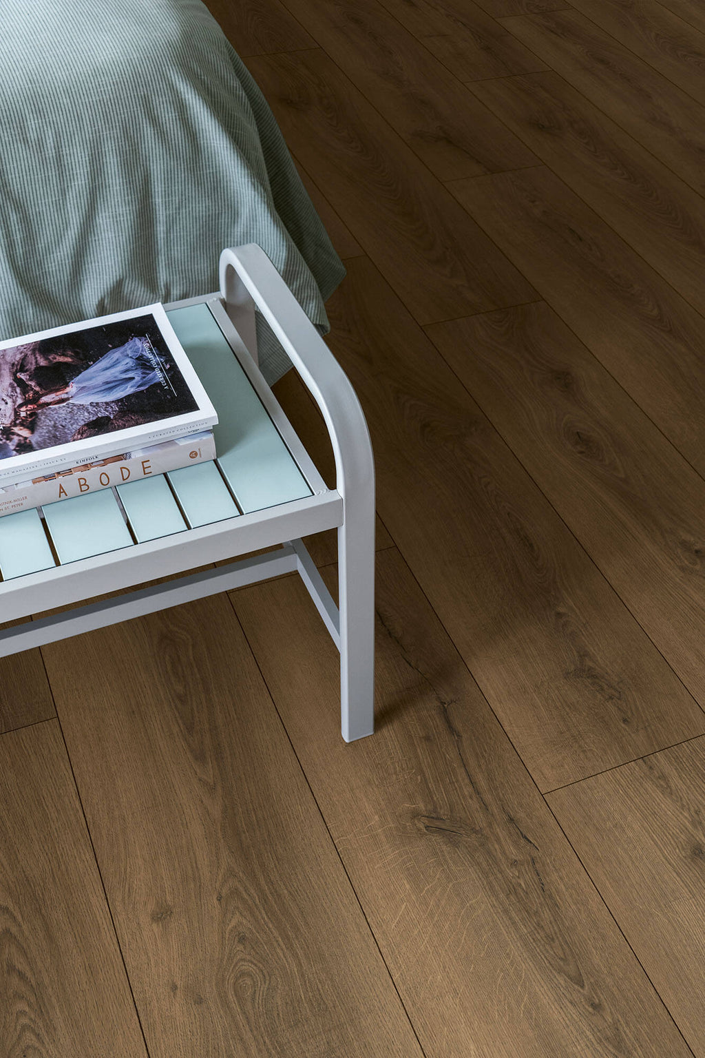 Small white side table with a green surface next to a bed on a wooden floor.
