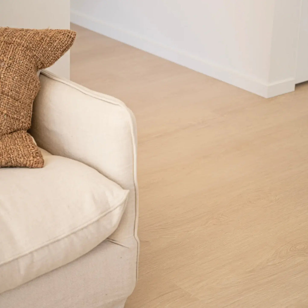 Beige carpeted floor with a corner of a beige sofa and a textured brown pillow.