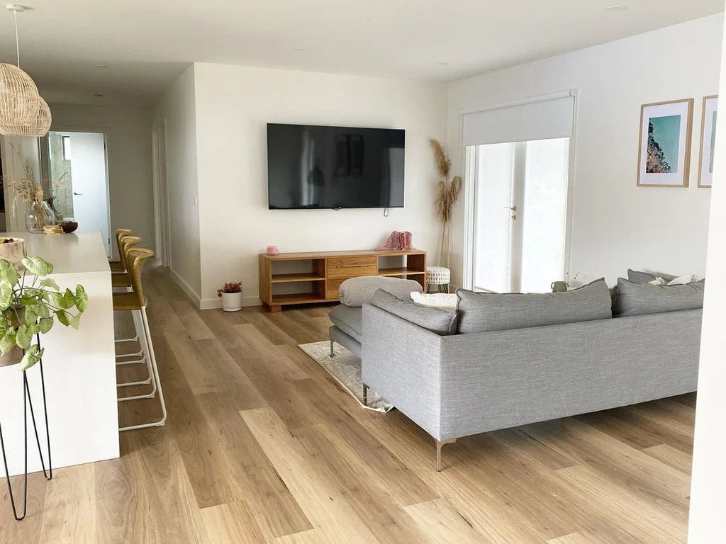 Modern living room with gray sofa, TV, and wooden floor.