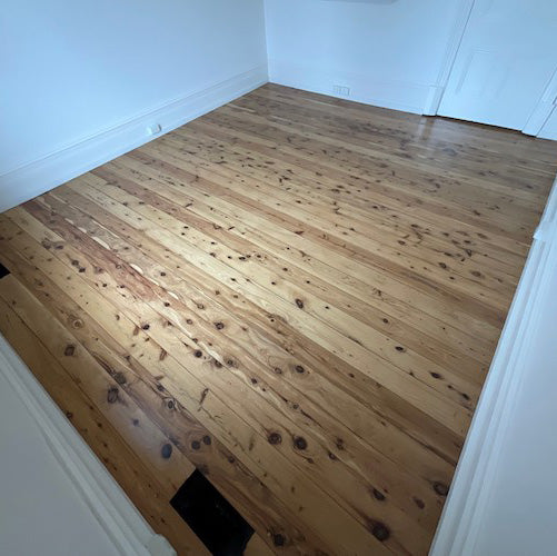Freshly sanded and polished Cypress Pine timber floorboards filling a bright, empty room in a classic Australian home, showcasing the species' signature warm honey tones, natural character knots, and rustic charm that only improves with age.