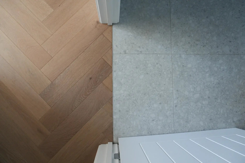 Wooden floor with a herringbone pattern next to a tiled wall and white radiator.