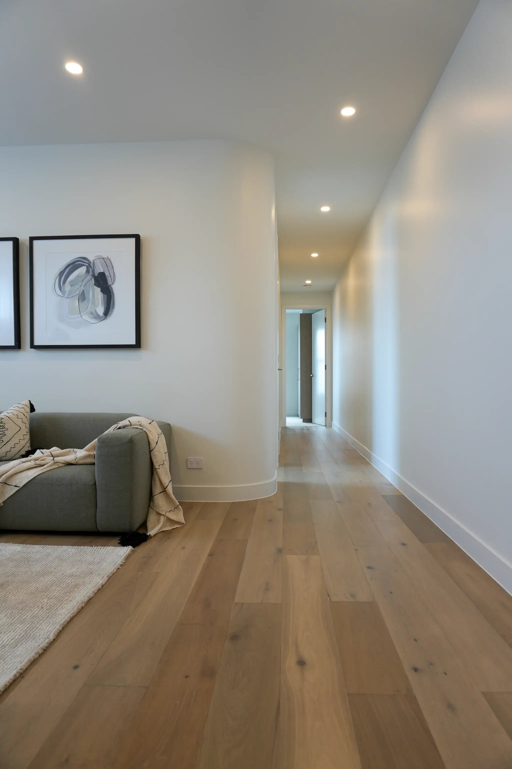 Modern living room with wooden floor, gray sofa, and framed artwork on white walls.