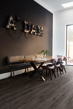 Modern dining area with wooden table and chairs against a dark wall with 'ADAM' letters.