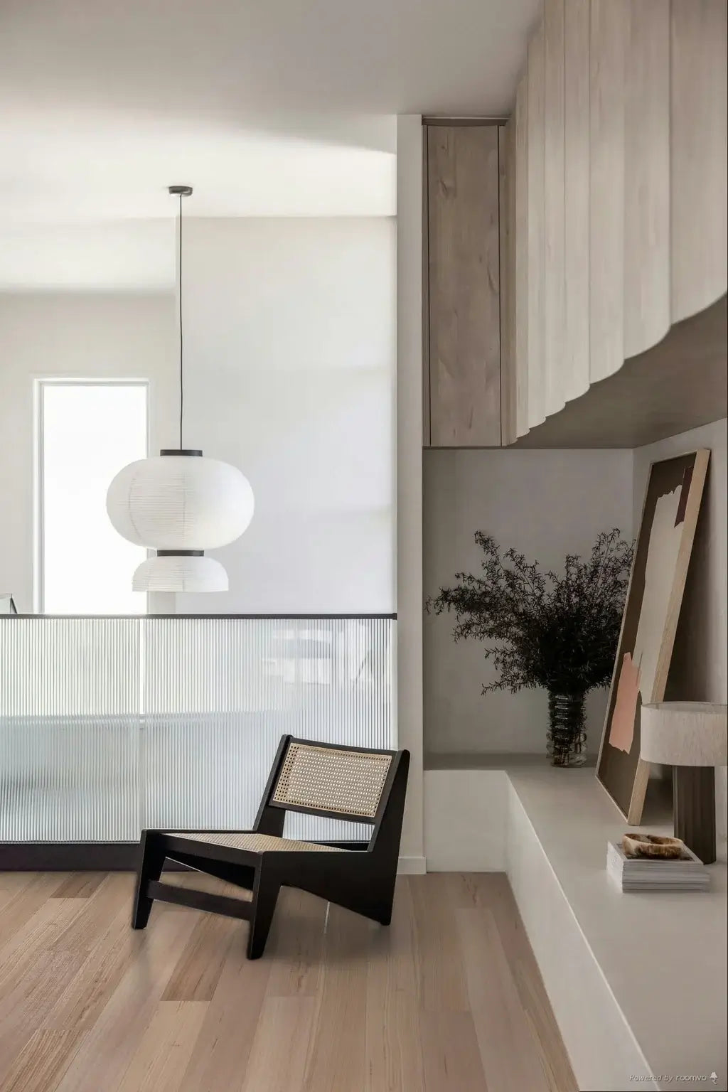 Modern interior with a black chair, white pendant light, and wooden cabinets.
