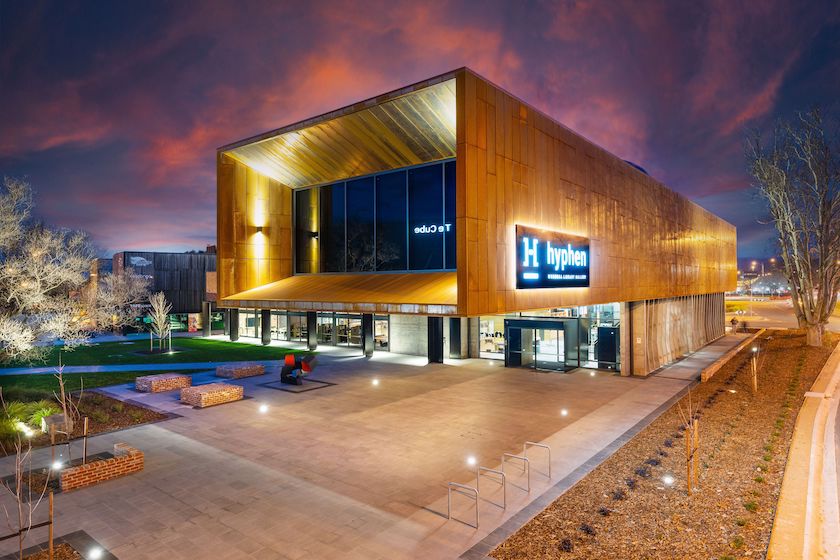 The striking Hyphen Wodonga Library and Gallery building photographed at dusk, its dramatic warm timber cladding facade glowing against a vivid sunset sky, showcasing the beauty and architectural impact of timber in large-scale commercial and public building projects.
