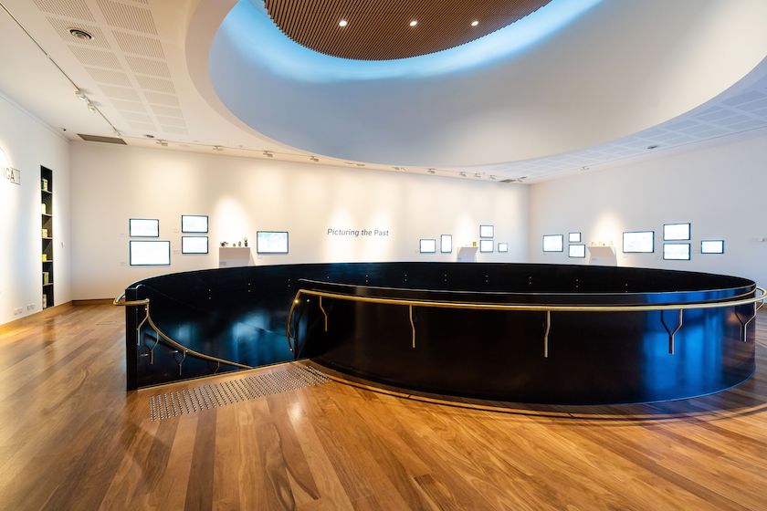 The gallery level of the Hyphen Wodonga Library and Gallery showcasing beautifully warm, polished hardwood timber flooring surrounding the dramatic black and brass spiral staircase void beneath a sweeping oval skylight, perfectly demonstrating how premium commercial timber flooring elevates the atmosphere of world-class public cultural spaces.