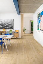 Light oak wood flooring in a modern, bright interior room with white walls, a dining table with blue chairs, and framed wall art.