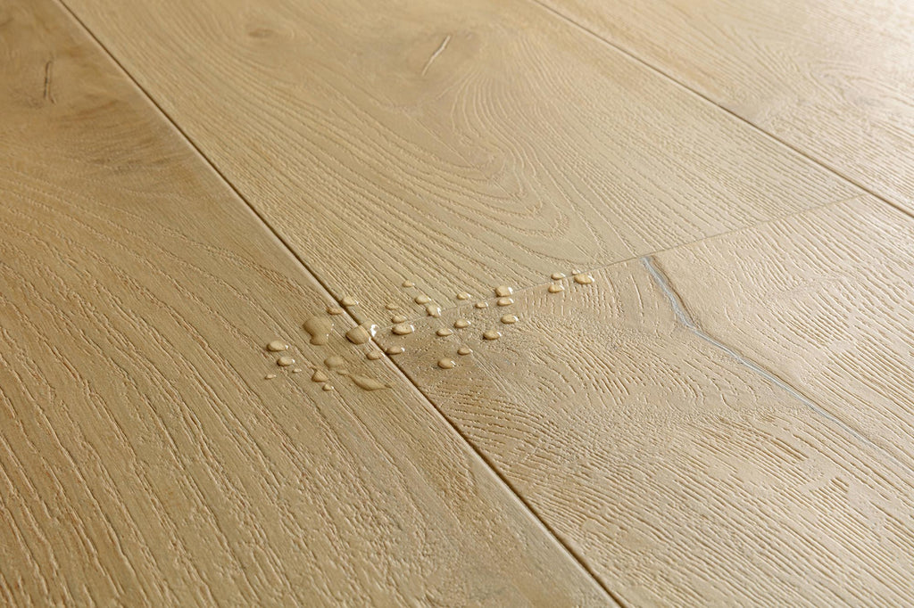Light oak wood flooring planks with visible grain and a small spill of water and debris near the center.
