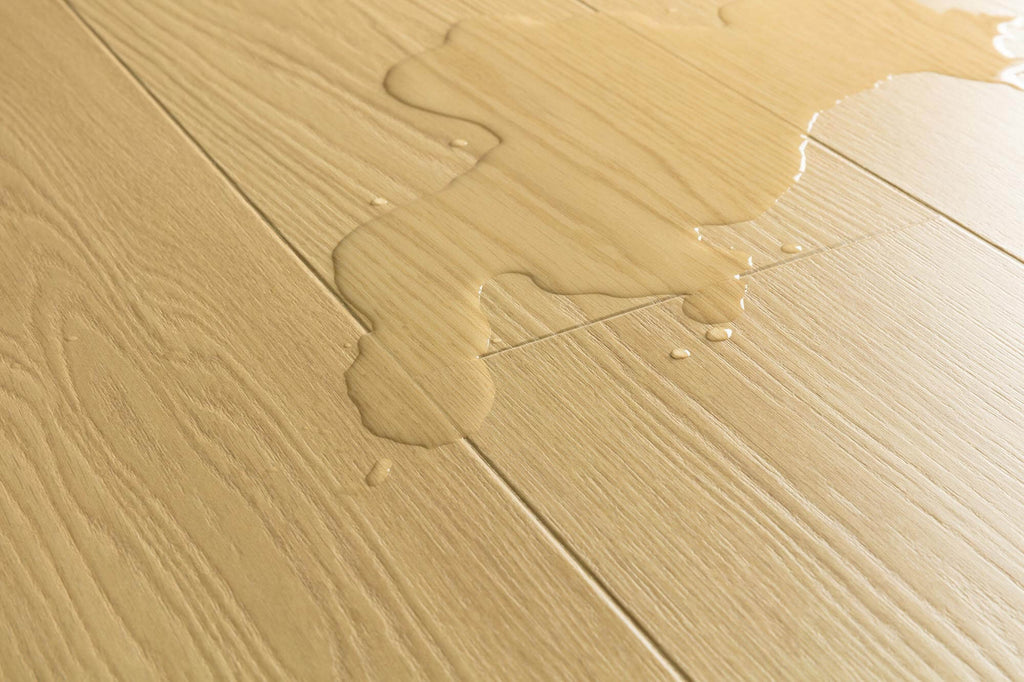 Close-up of light beige wood-look flooring with a glossy liquid spill running across the surface.