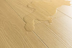 Close-up of light beige wood-look flooring with a glossy liquid spill running across the surface.