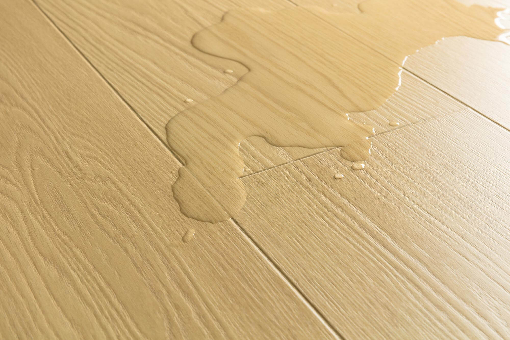 Close-up of light beige wood-look flooring with a glossy liquid spill running across the surface.