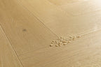 Light oak wood flooring planks arranged in a herringbone pattern, with a small cluster of broken glass chips on the surface.