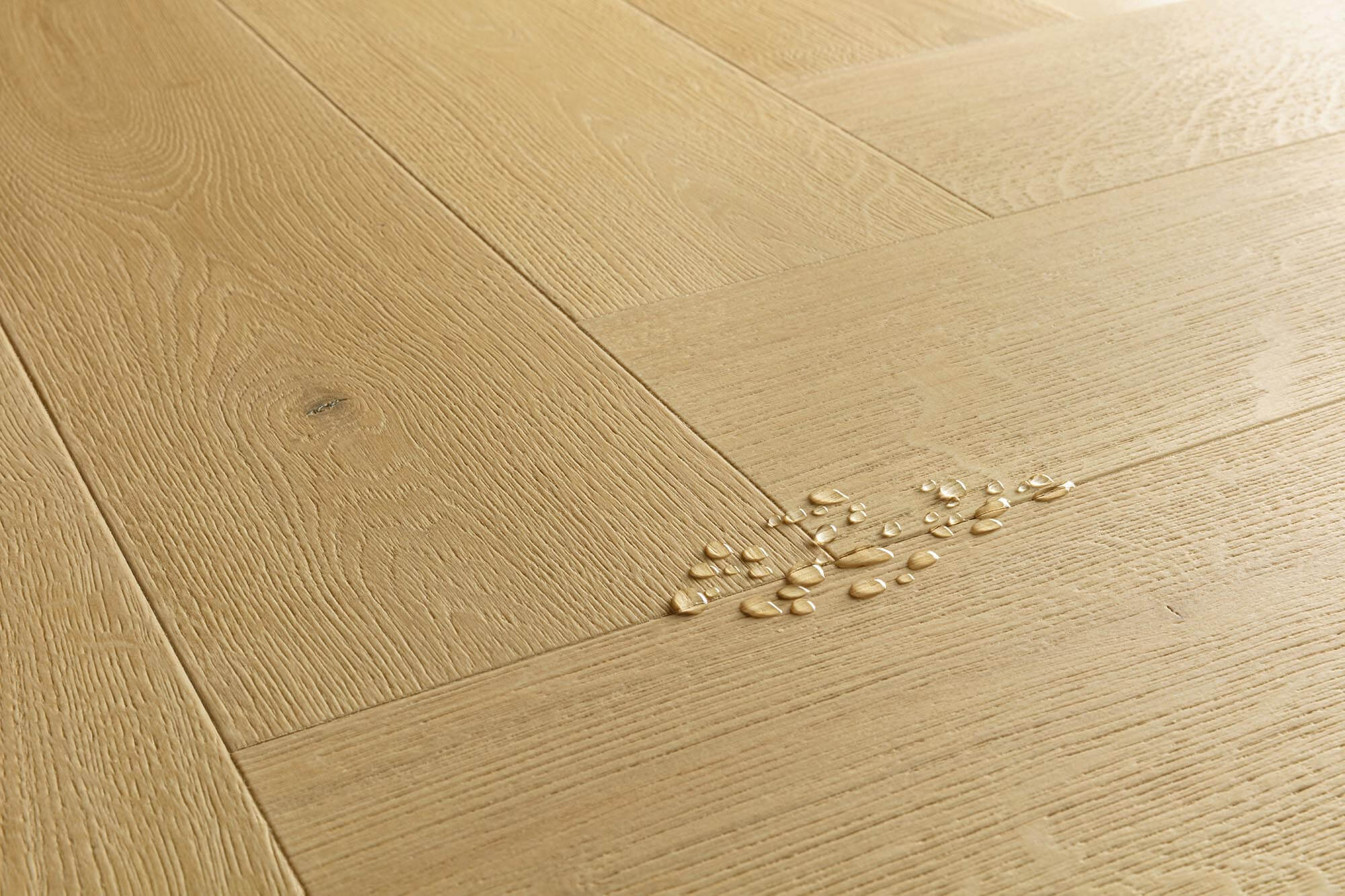 Light oak wood flooring planks arranged in a herringbone pattern, with a small cluster of broken glass chips on the surface.