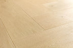 Light natural oak wood flooring planks arranged in a herringbone pattern, showing detailed wood grain and subtle knots.