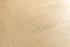 Light natural oak wood flooring planks arranged in a herringbone pattern, with a small cluster of scattered wood shavings on the surface.