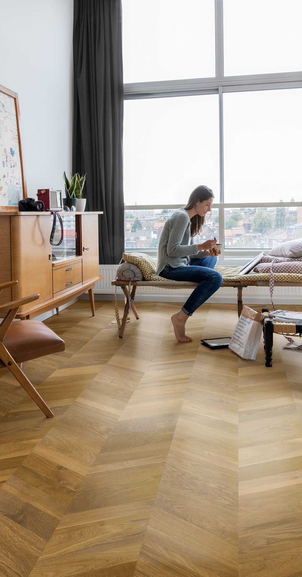 Woman sitting on a wooden floor in a modern living room with large windows.