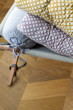 Close-up of a wooden stool with patterned cushions on a wooden floor.