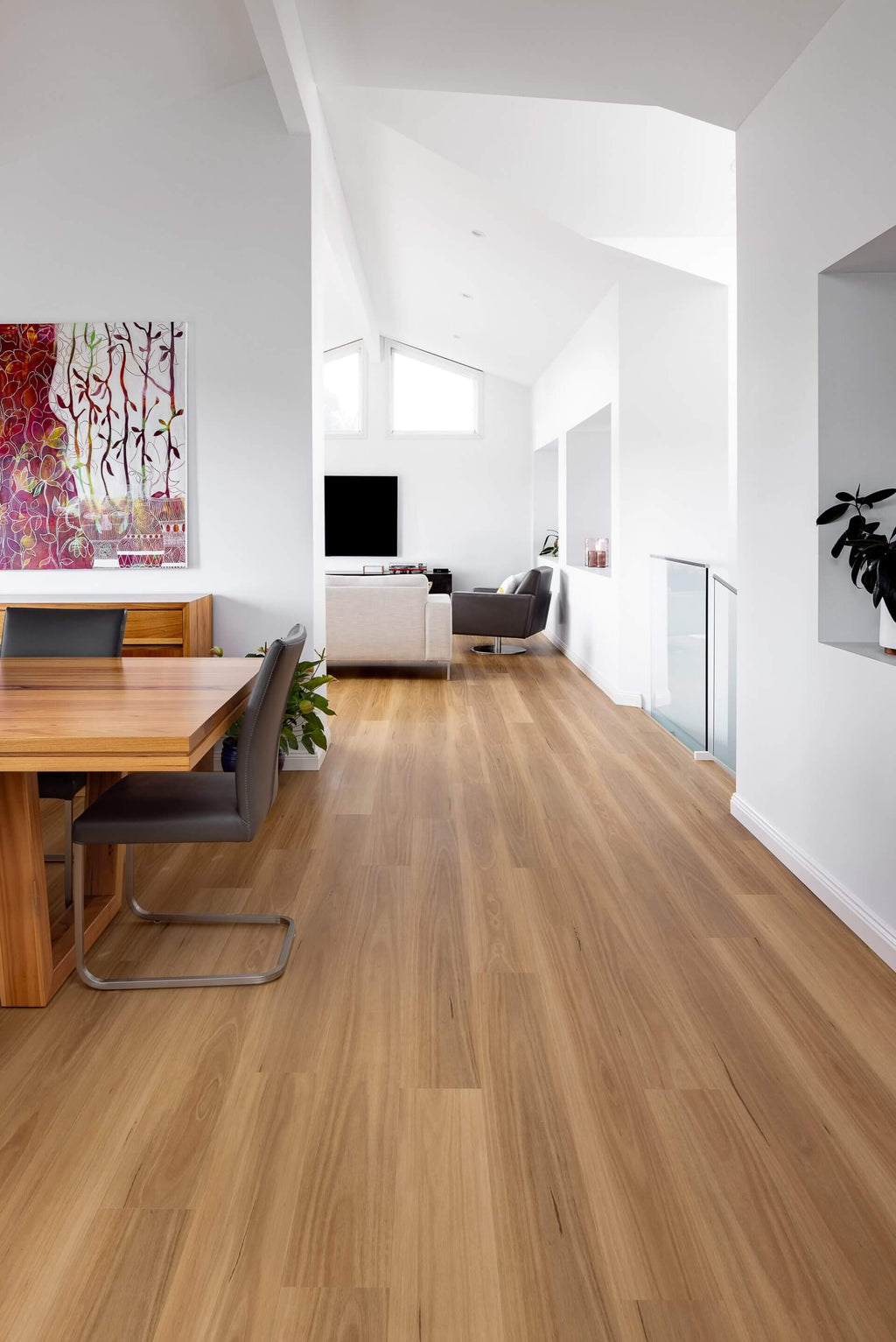 Light brown wood laminate flooring shown in a modern, bright white living room with a dining table, chairs, and a living room in the background.