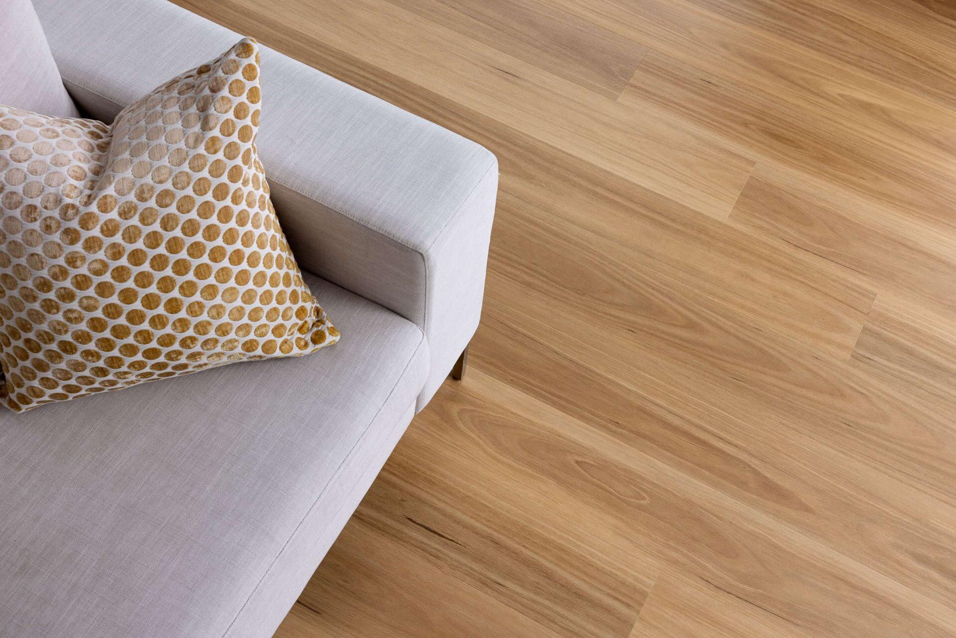 Light oak wood plank flooring shown in a modern living room setting next to a light gray sofa with a patterned throw pillow.