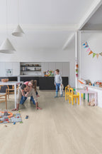 Family playing on a light wood floor in a modern kitchen and living area.