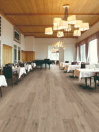 Large room with wooden flooring, tables, chairs, and chandeliers.