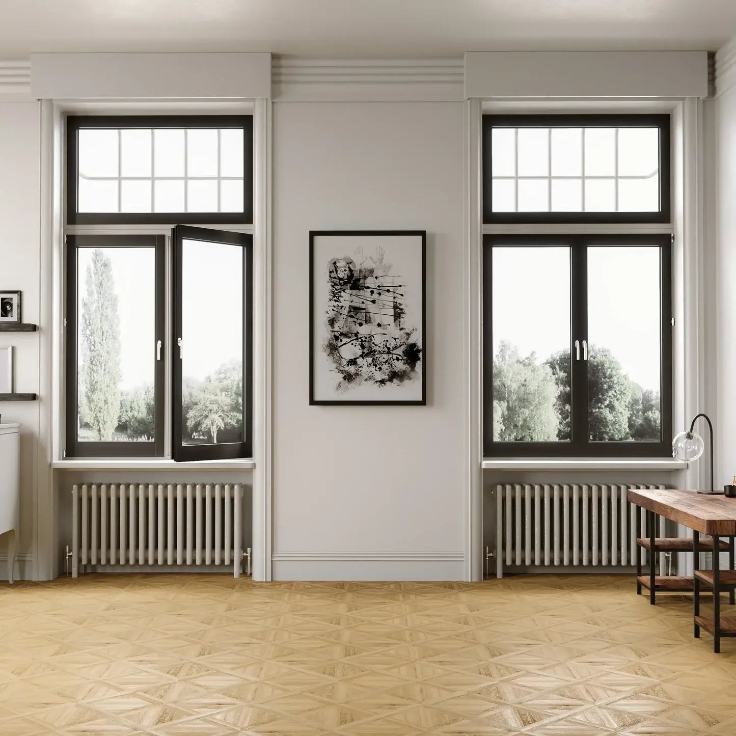 A modern interior room with two tall black-framed windows, a central framed black-and-white artwork on a white wall, radiators beneath the windows, a light wood floor, and part of a wooden desk on the right.