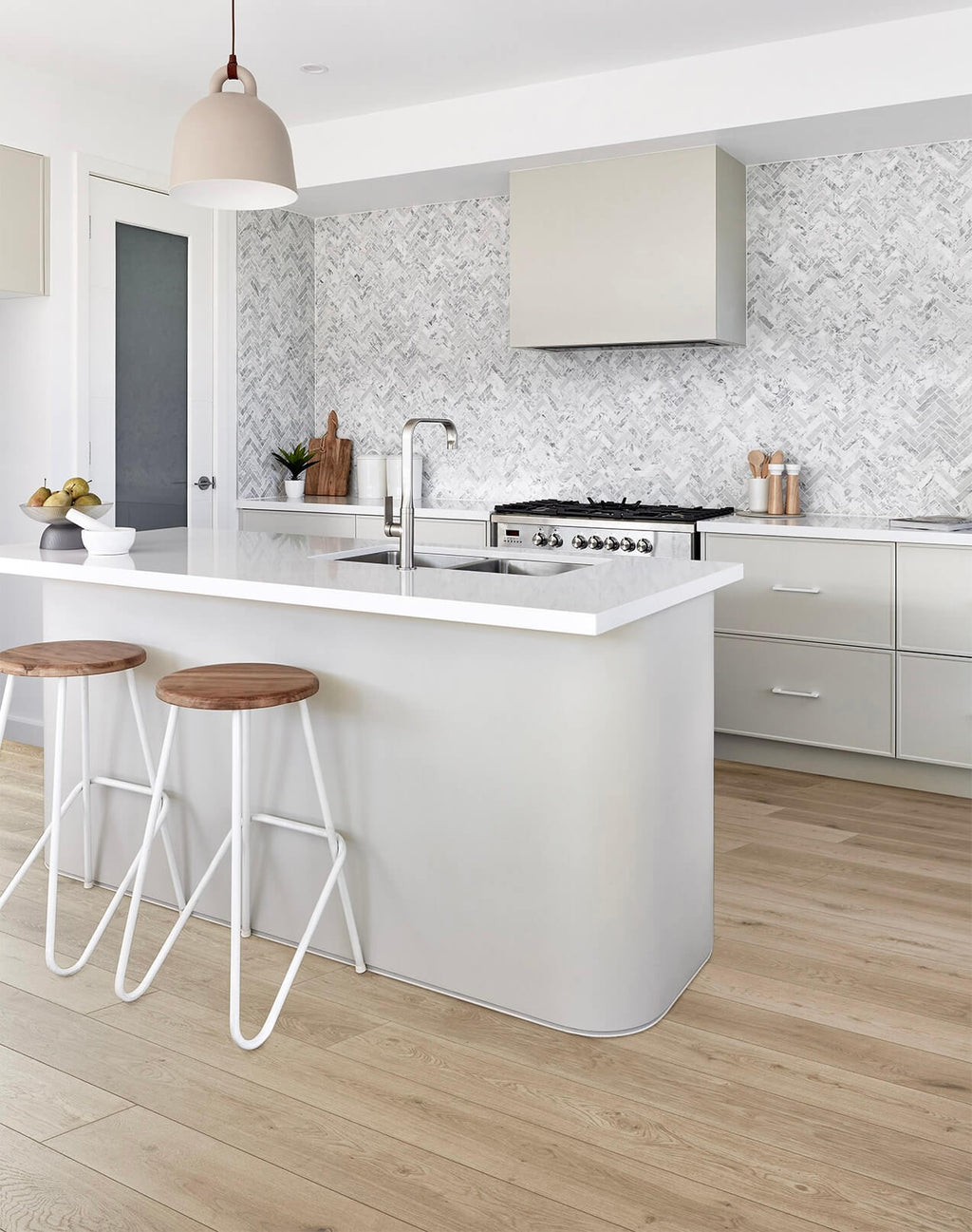 Modern kitchen with white island, wooden stools, and light wood flooring.