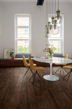 Modern dining room with round white table and yellow chairs, large windows, and pendant lights.