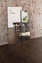 Full-length mirror leaning against a brick wall reflecting a dining area.