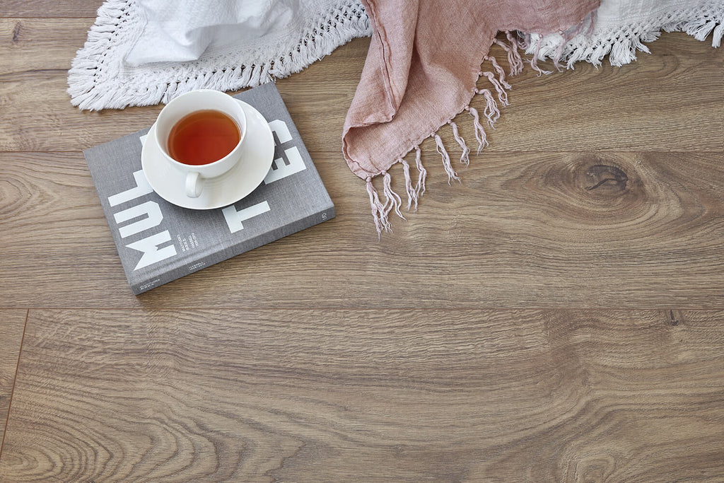 Teacup with saucer on a magazine on a wooden surface with a pink blanket.