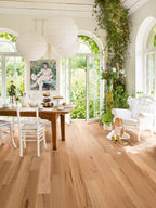 Brightly lit room with wooden floor, dining table, and large windows.