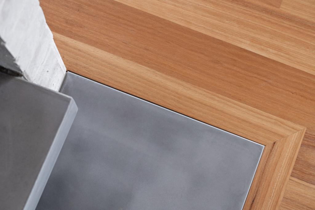 A close-up detail shot of a precision timber floor installation showing the immaculate transition between warm Australian hardwood timber flooring and a steel fireplace hearth plate, highlighting the exceptional craftsmanship and fine finishing work that goes into a professional timber floor installation.