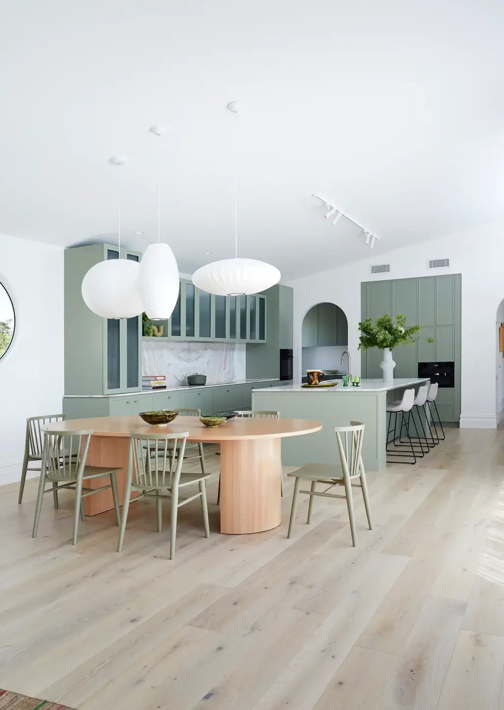 Modern kitchen with wooden dining table and chairs, light green walls, and white ceiling.