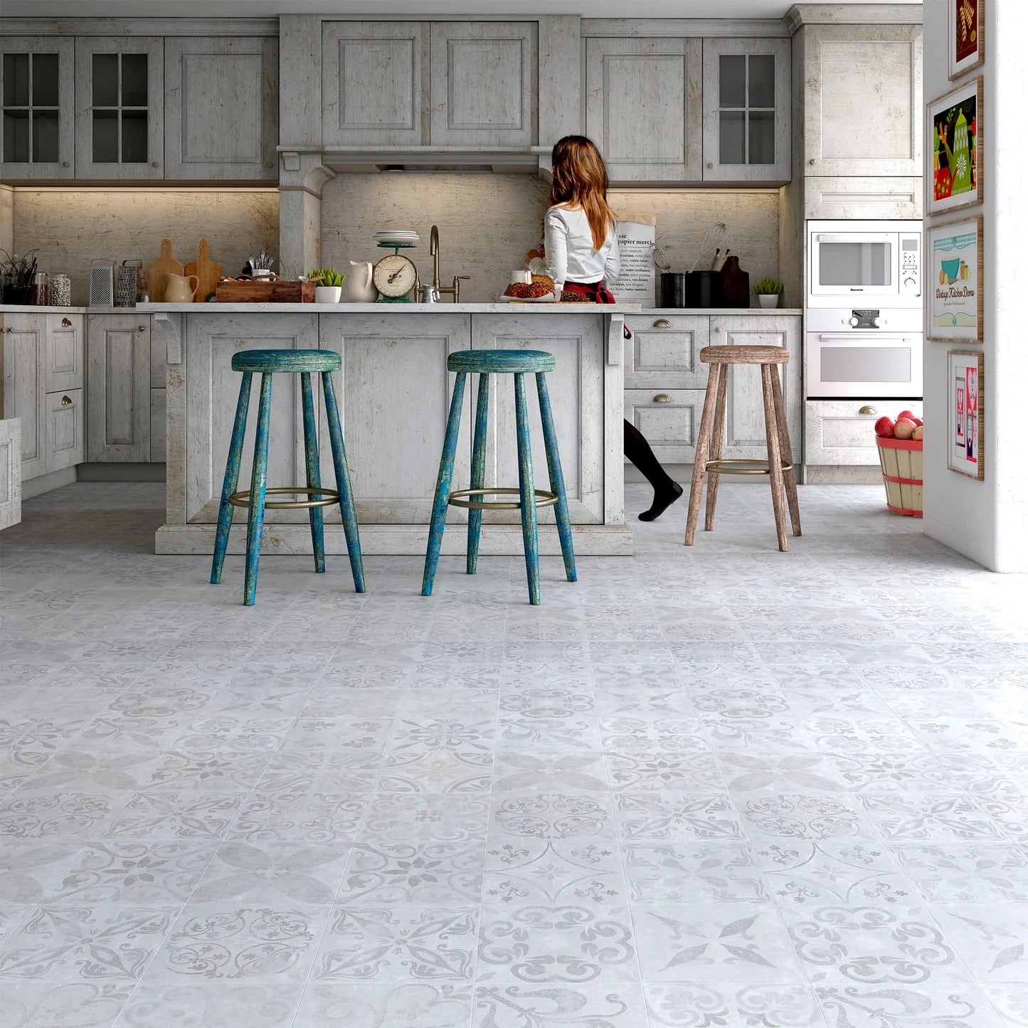 A wide interior kitchen scene with pale gray patterned flooring, white cabinets, two teal bar stools at the island, and a woman standing near the counter.