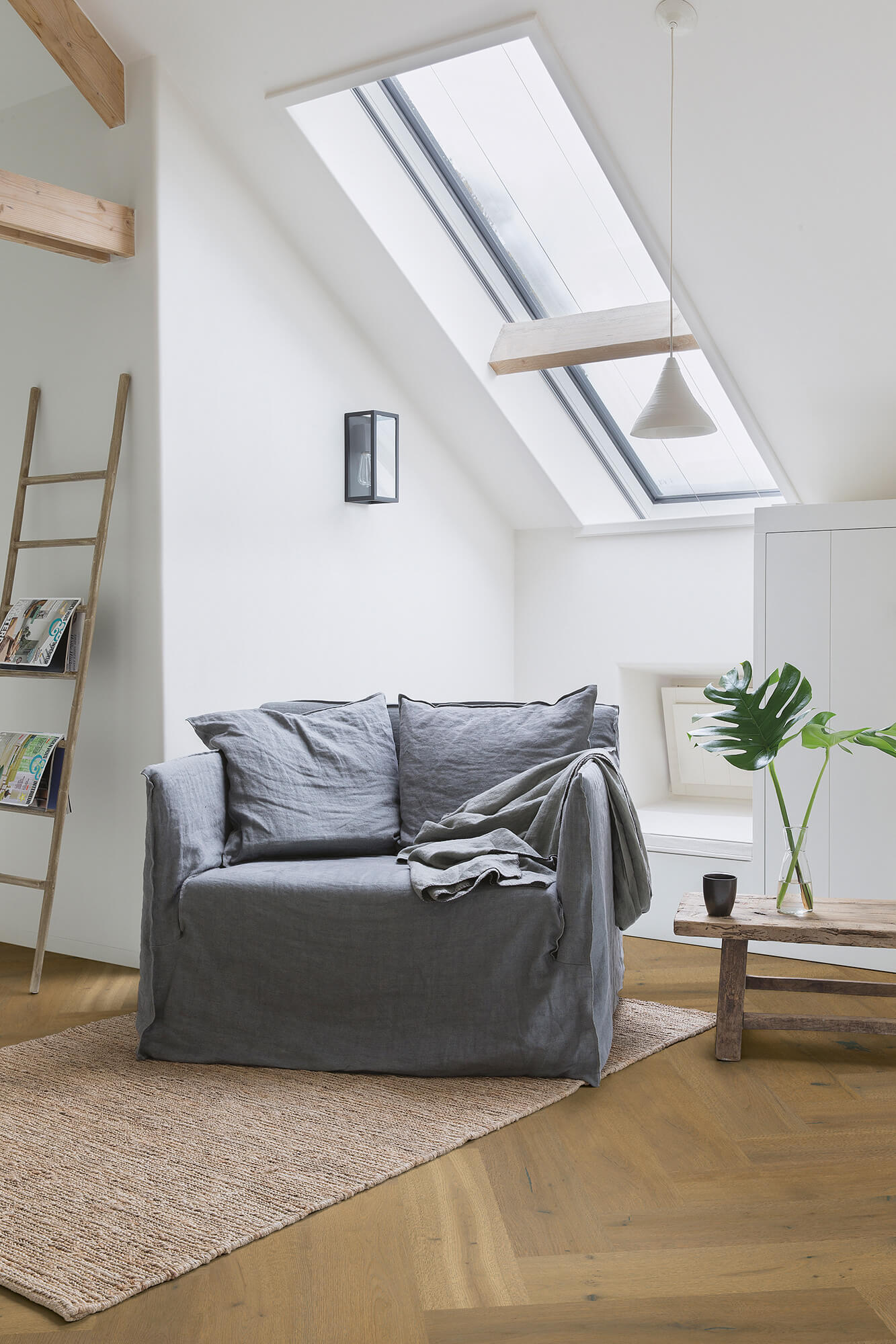 Modern living room with gray sofa, skylights, and wooden floor.
