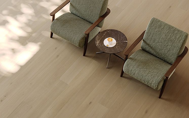 Two green armchairs with wooden frames on a light wood floor.