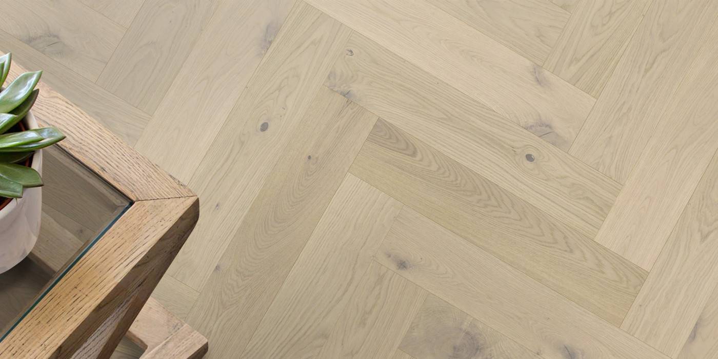 Wooden floor with a herringbone pattern and a small plant on a wooden table.
