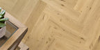 Wooden floor with herringbone pattern and a small plant on a wooden surface.