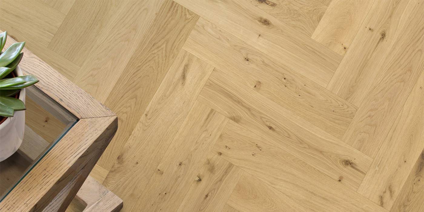 Wooden floor with herringbone pattern and a small plant on a wooden surface.