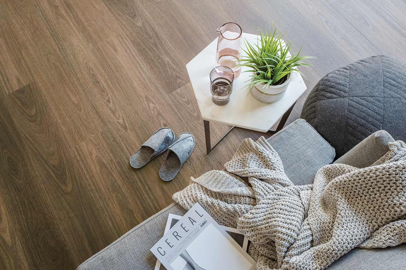 Living room with a gray sofa, wooden floor, and small table with glasses and a plant.